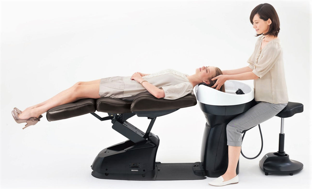 Stylist seated behind a reclining client on a Takara Belmont YUME Espoir shampoo unit